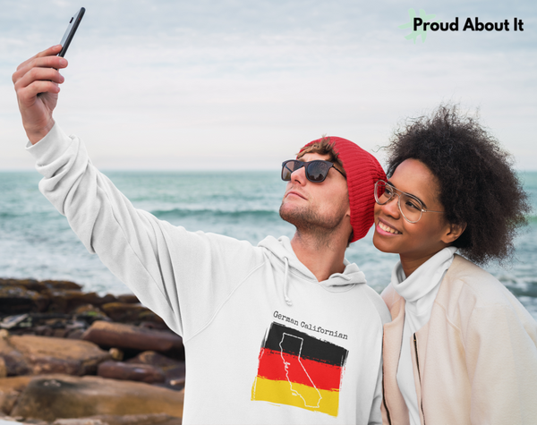 man taking a selfie on the beach with friend wearing a white German Californian Unisex Hoodie | German Heritage, California Style